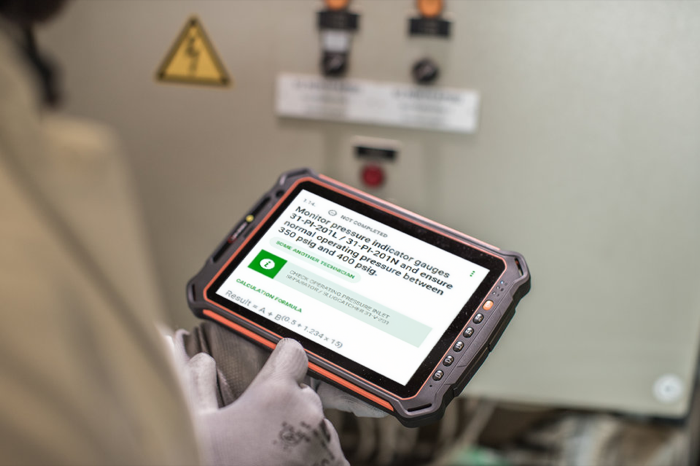 A gloved hand holding a rugged tablet running Operator Workbench, showing a pressure gauge check on a live site